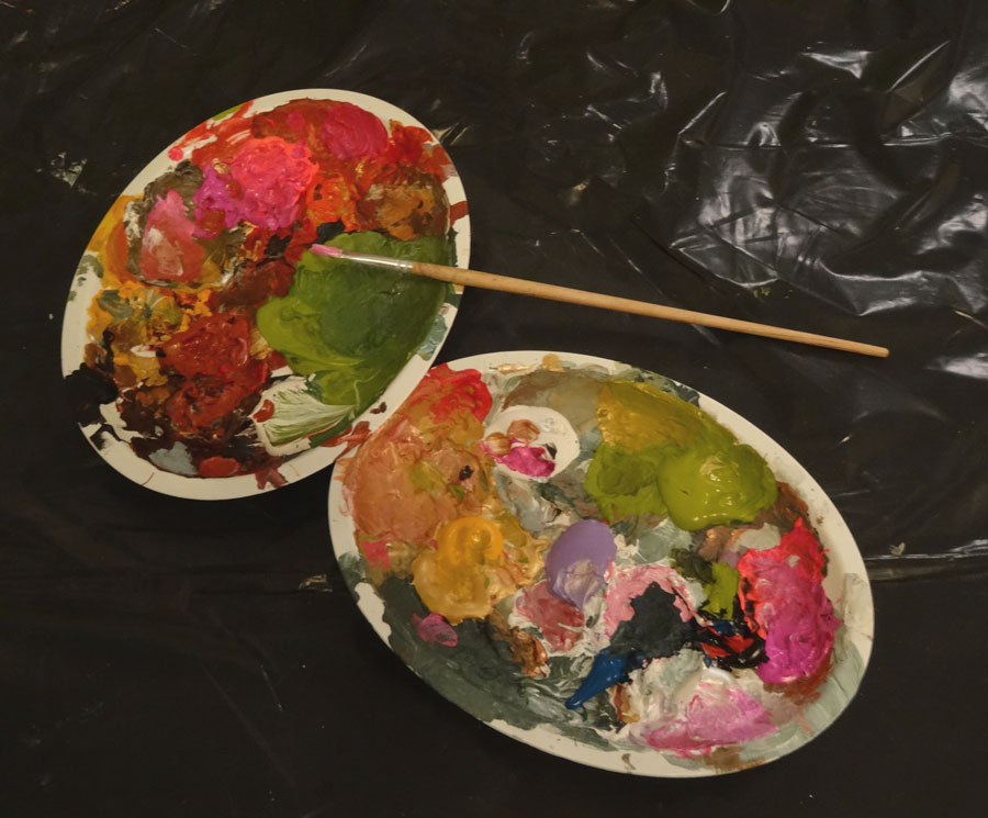 Zwei ovale Farbpaletten mit bunten Farben und einem Pinsel auf schwarzer Oberfläche.