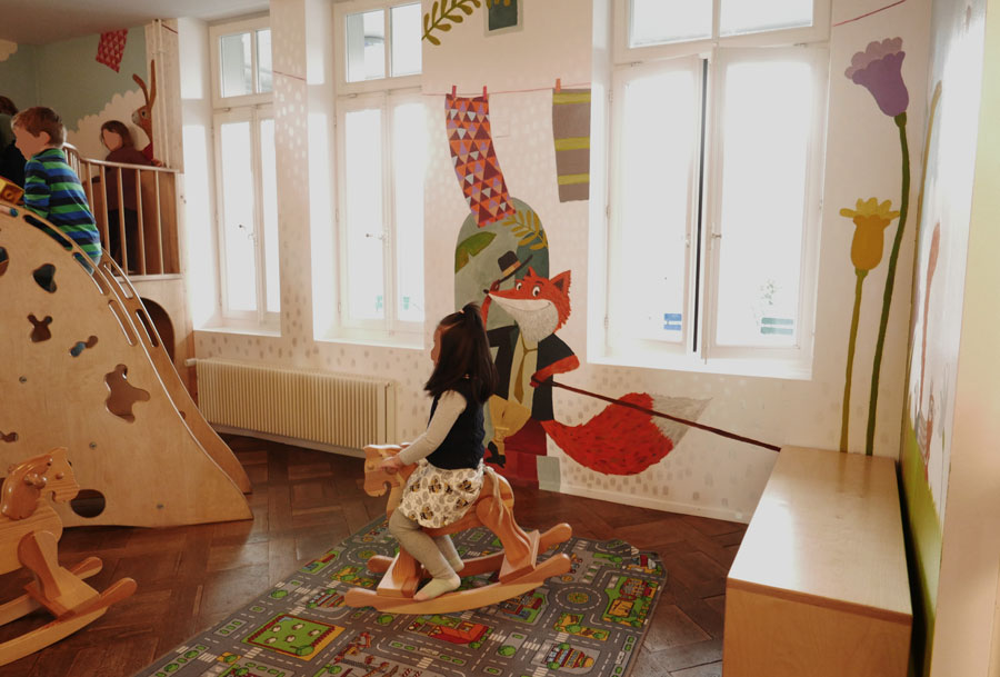 Wandmalerei mit Fuchs in Kleidung, bunte Textilien, Blumen und geometrische Formen. Farbenfrohe, kindergerechte Illustrationen.