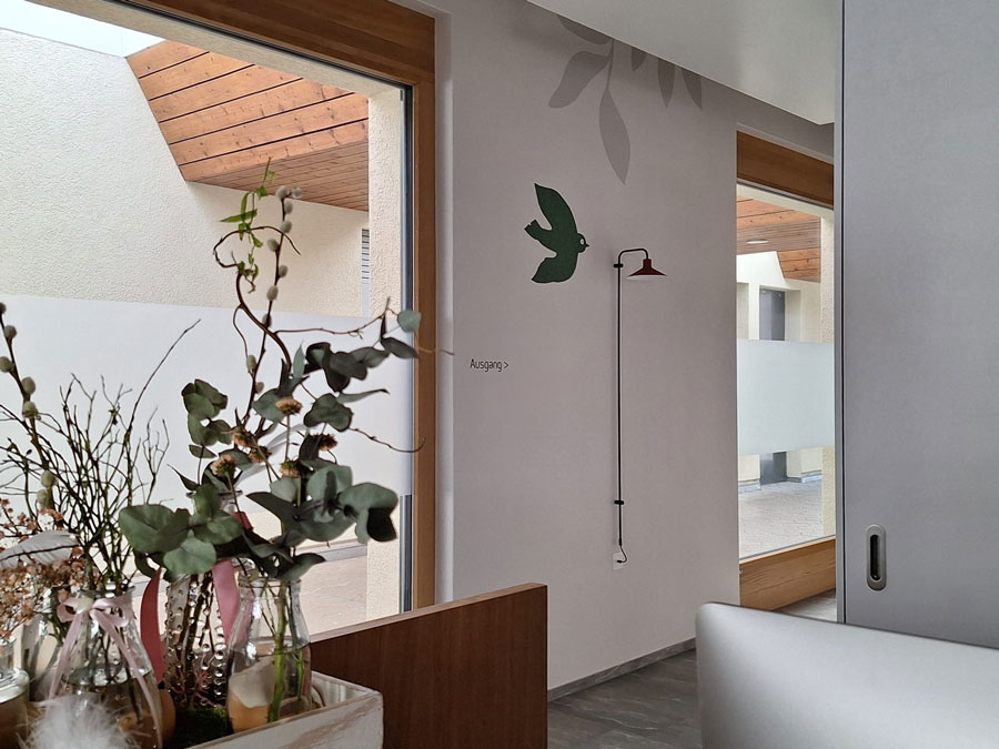 Wandmalerei mit grünem Vogel, roten Schirm-Lampe und grauem Blatt im minimalistischen Design. Text 