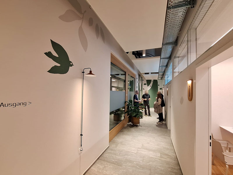 Wandmalerei mit grünem Vogel und Blättern auf hellem Hintergrund; stilisierte Naturmotive dekorieren die Flurwand.