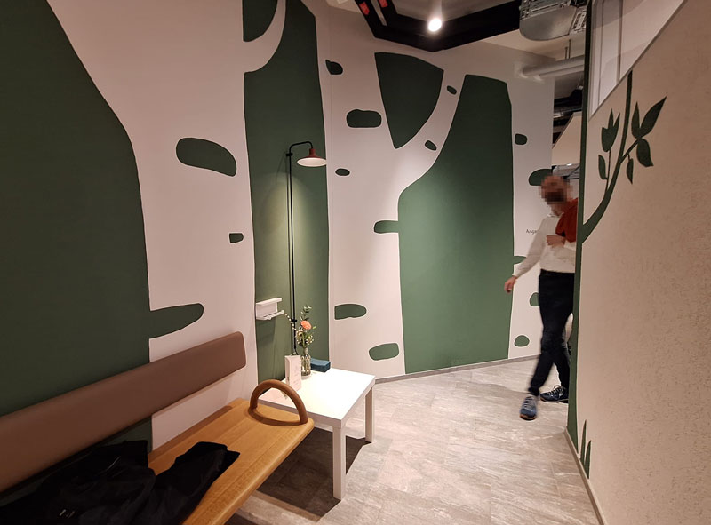 Wandmalerei mit weißen Birkenstämmen und grünen Blättern auf dunklem Hintergrund.