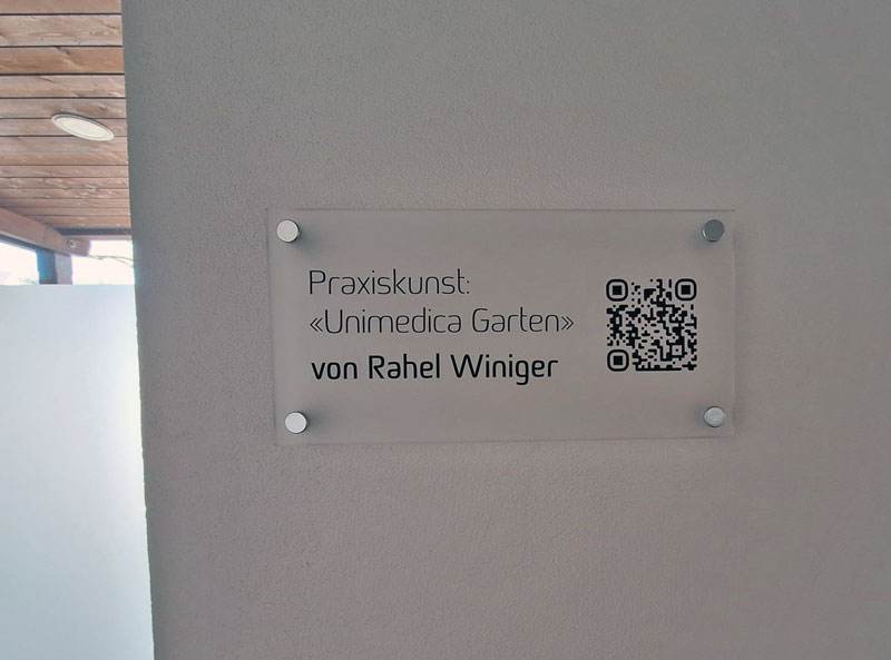 Glastafel mit Text „Praxiskunst: Unimedica Garten“ und QR-Code, Verweist auf Arbeiten von Rahel Winiger.